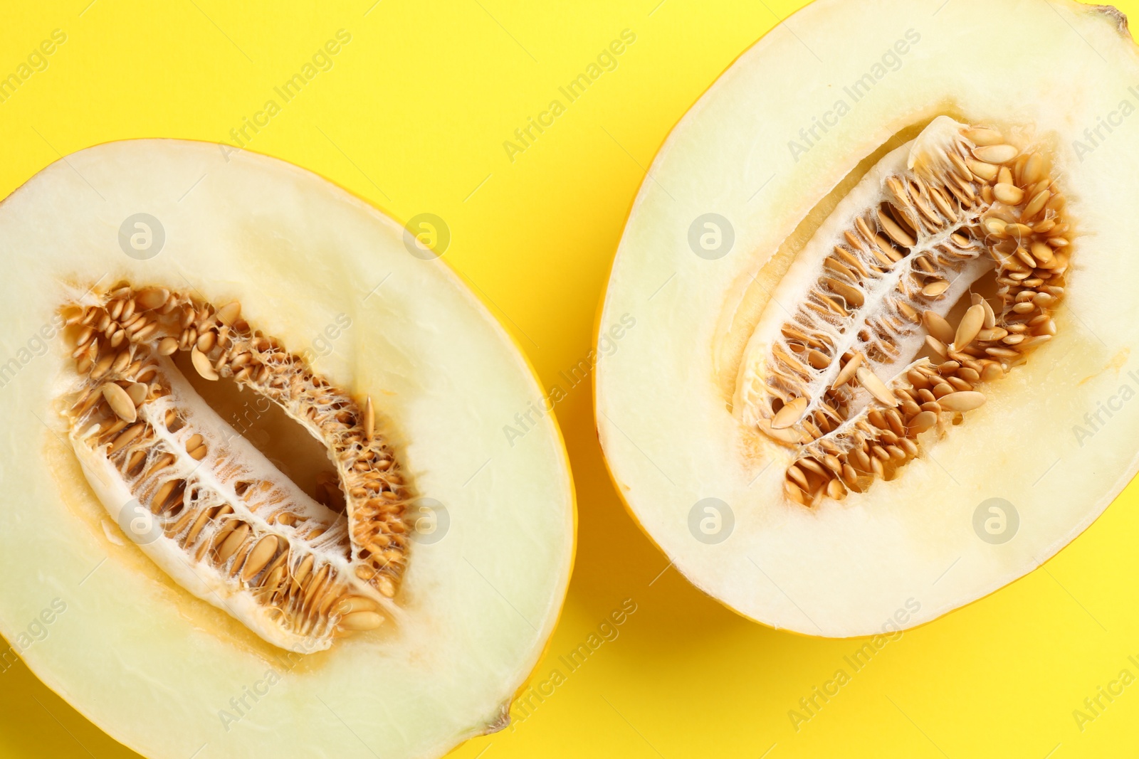 Photo of Halves of fresh melon on yellow background, top view