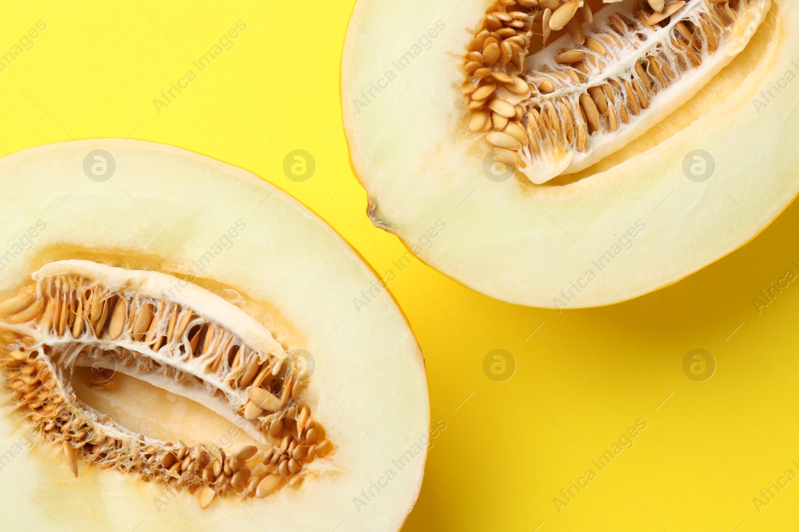 Photo of Halves of fresh melon on yellow background, top view