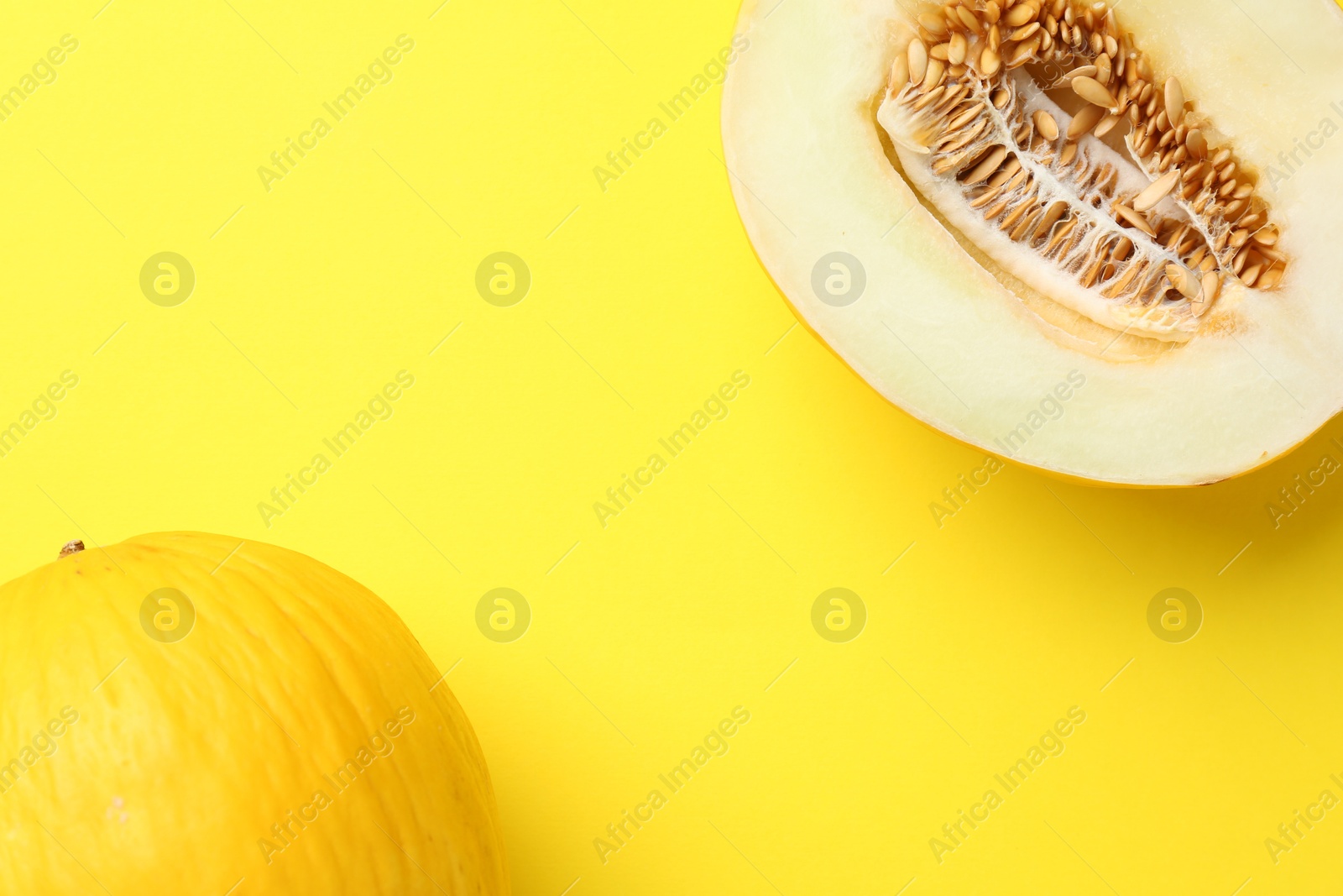 Photo of Whole and half of fresh melon on yellow background, flat lay