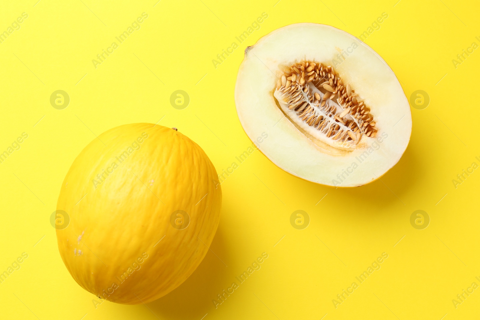 Photo of Whole and half of fresh melon on yellow background, flat lay