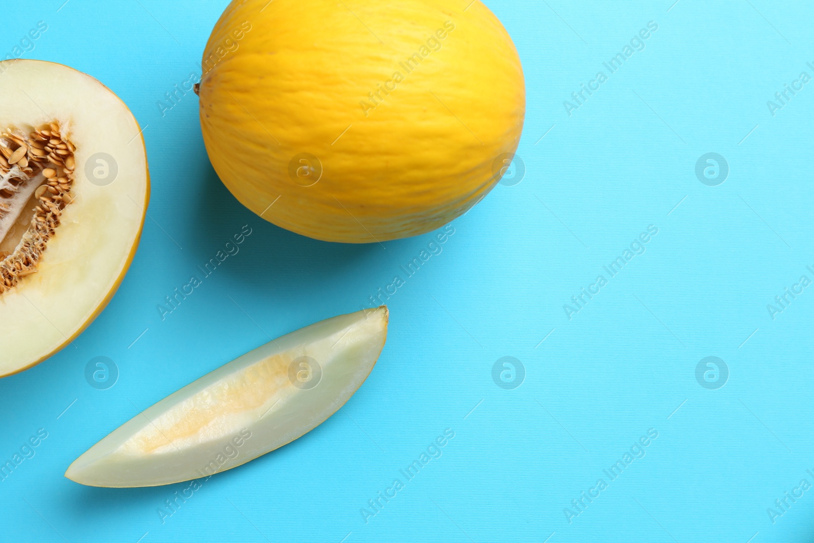 Photo of Whole and cut melons on light blue background, flat lay. Space for text