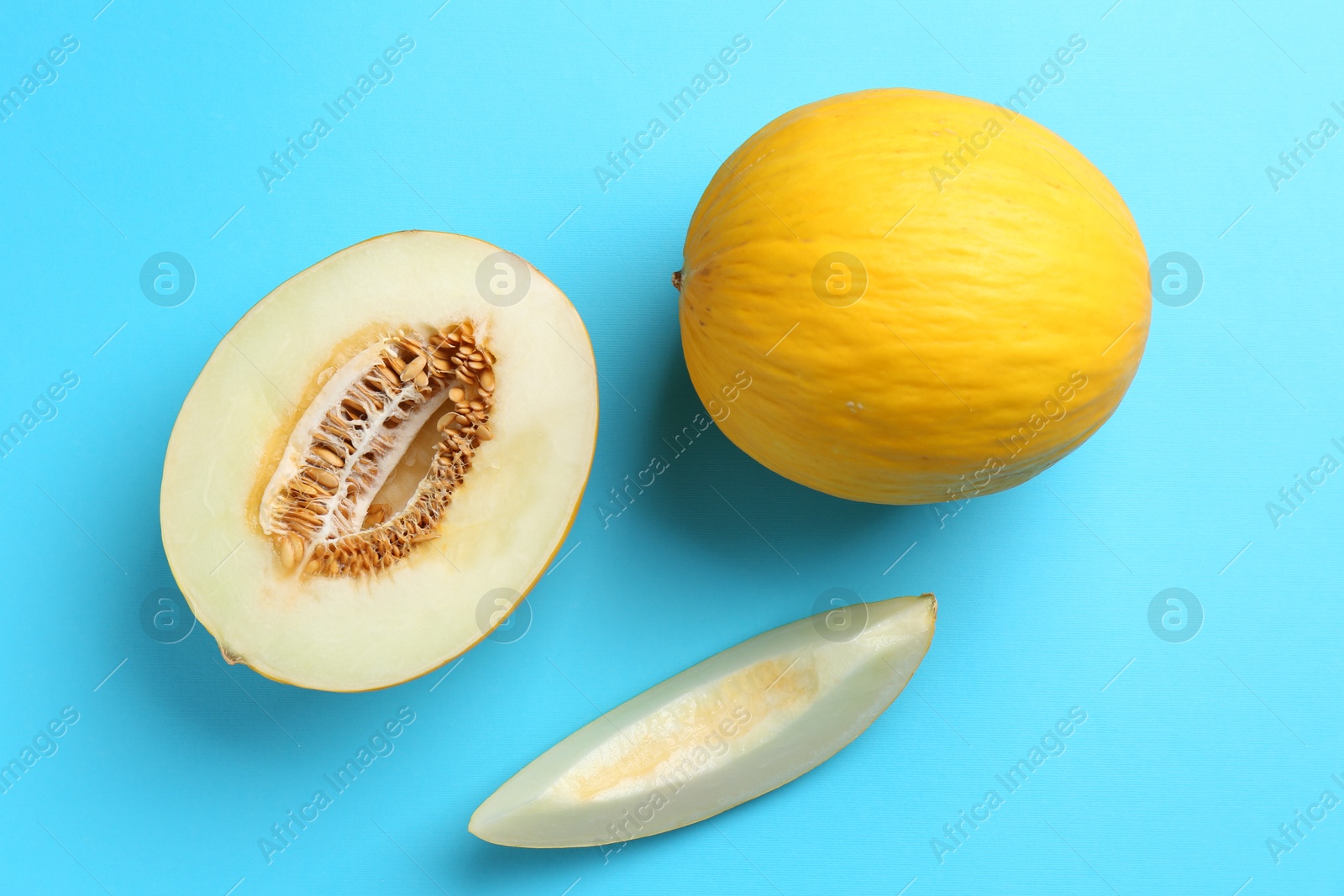 Photo of Whole and cut melons on light blue background, flat lay