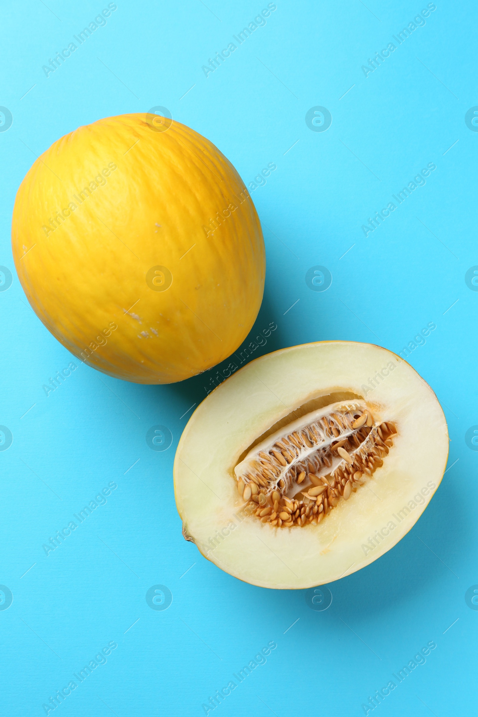 Photo of Whole and half of fresh melon on light blue background, flat lay