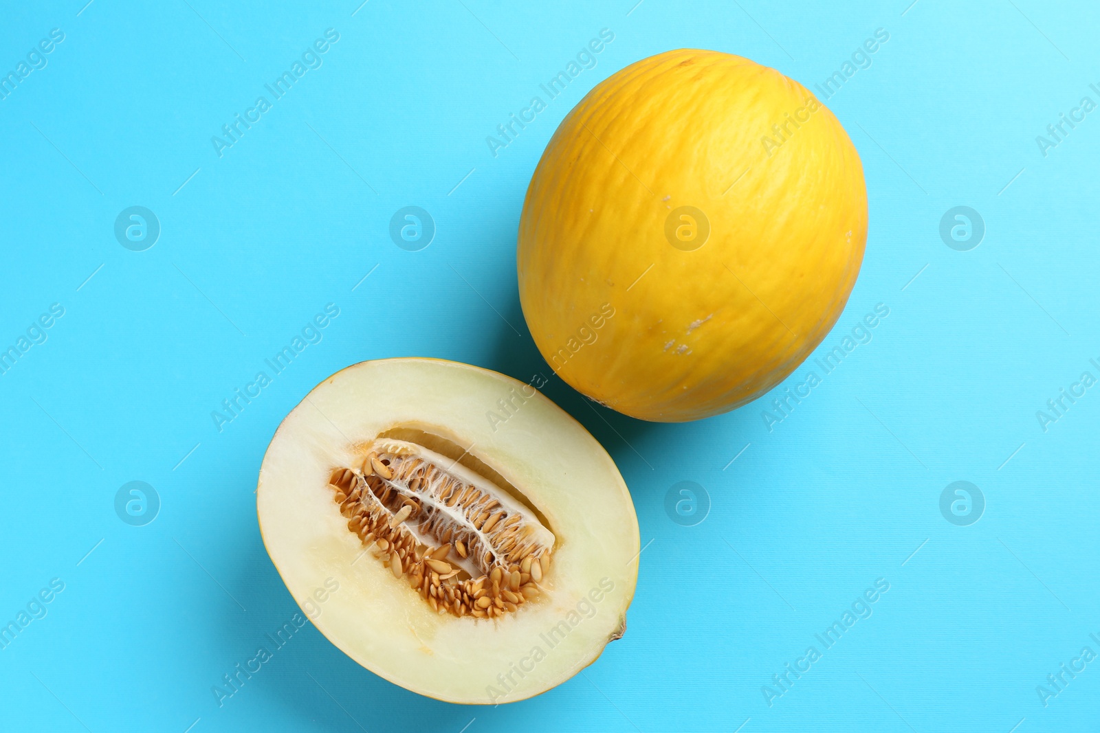 Photo of Whole and half of fresh melon on light blue background, flat lay