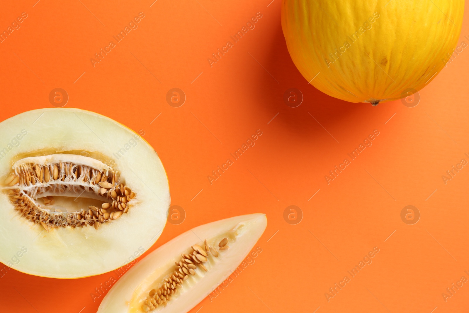 Photo of Whole and cut melons on orange background, flat lay