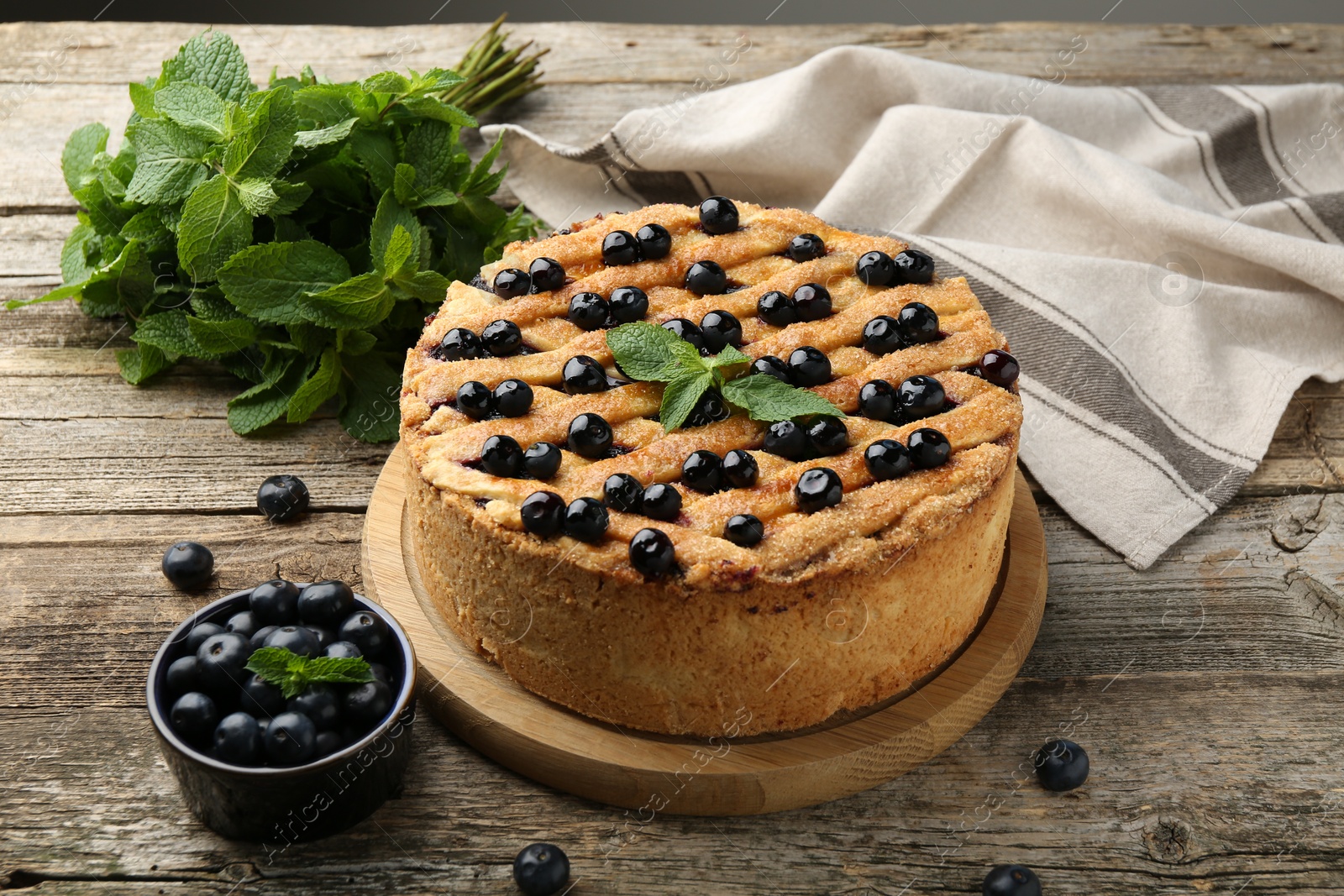 Photo of Delicious homemade blueberry pie with mint and fresh berries on wooden table