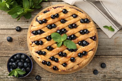 Photo of Delicious homemade blueberry pie with mint and fresh berries on wooden table, top view