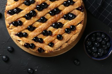 Photo of Delicious homemade blueberry pie and fresh berries on black table, top view