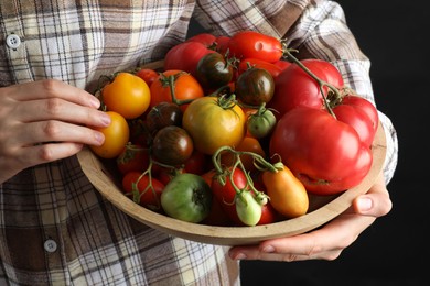 Photo of Woman holding bowl of different fresh tomatoes on black background, closeup