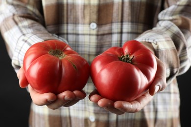 Photo of Woman holding fresh ripe tomatoes on black background, closeup