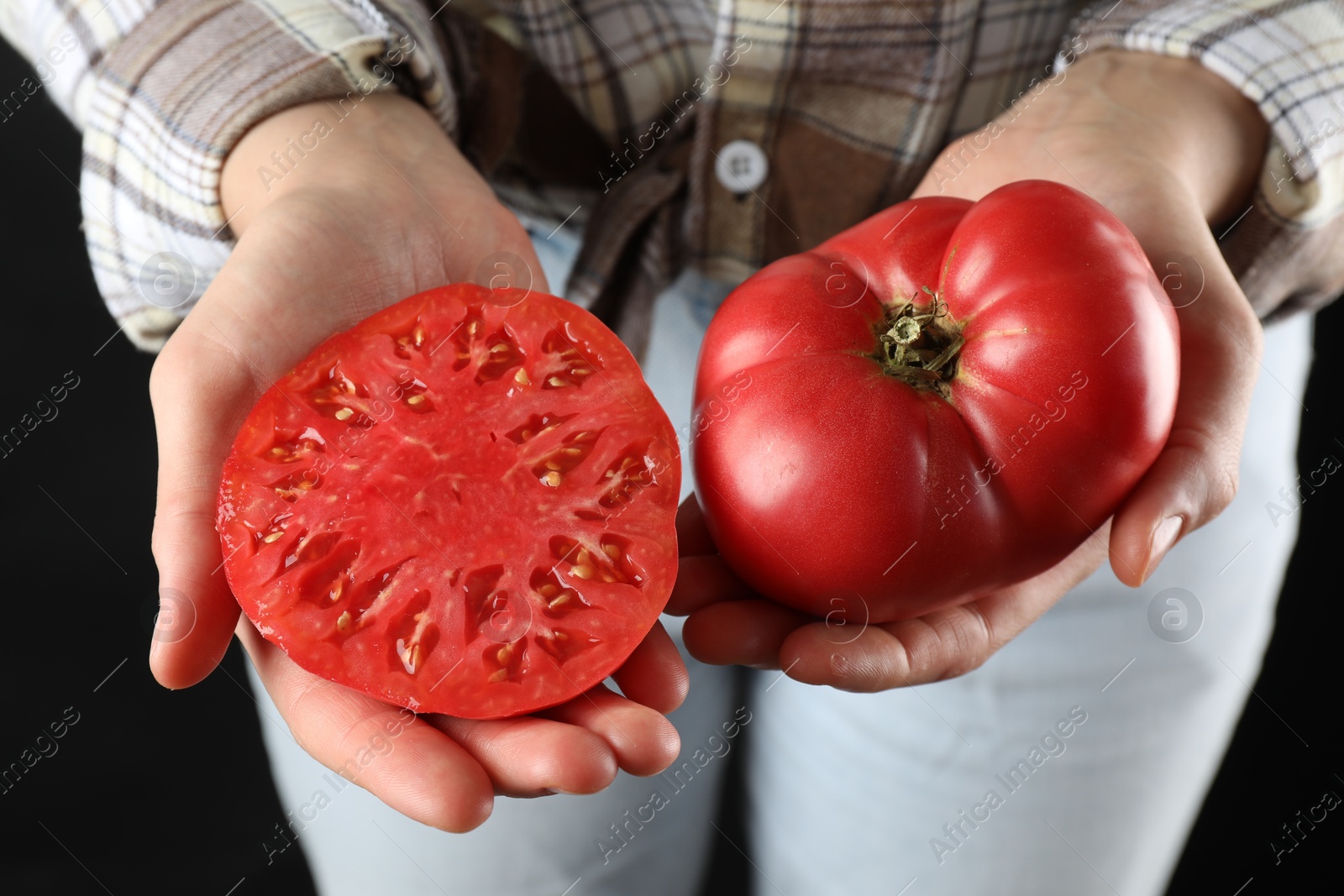 Photo of Woman holding whole and cut ripe tomatoes on black background, closeup