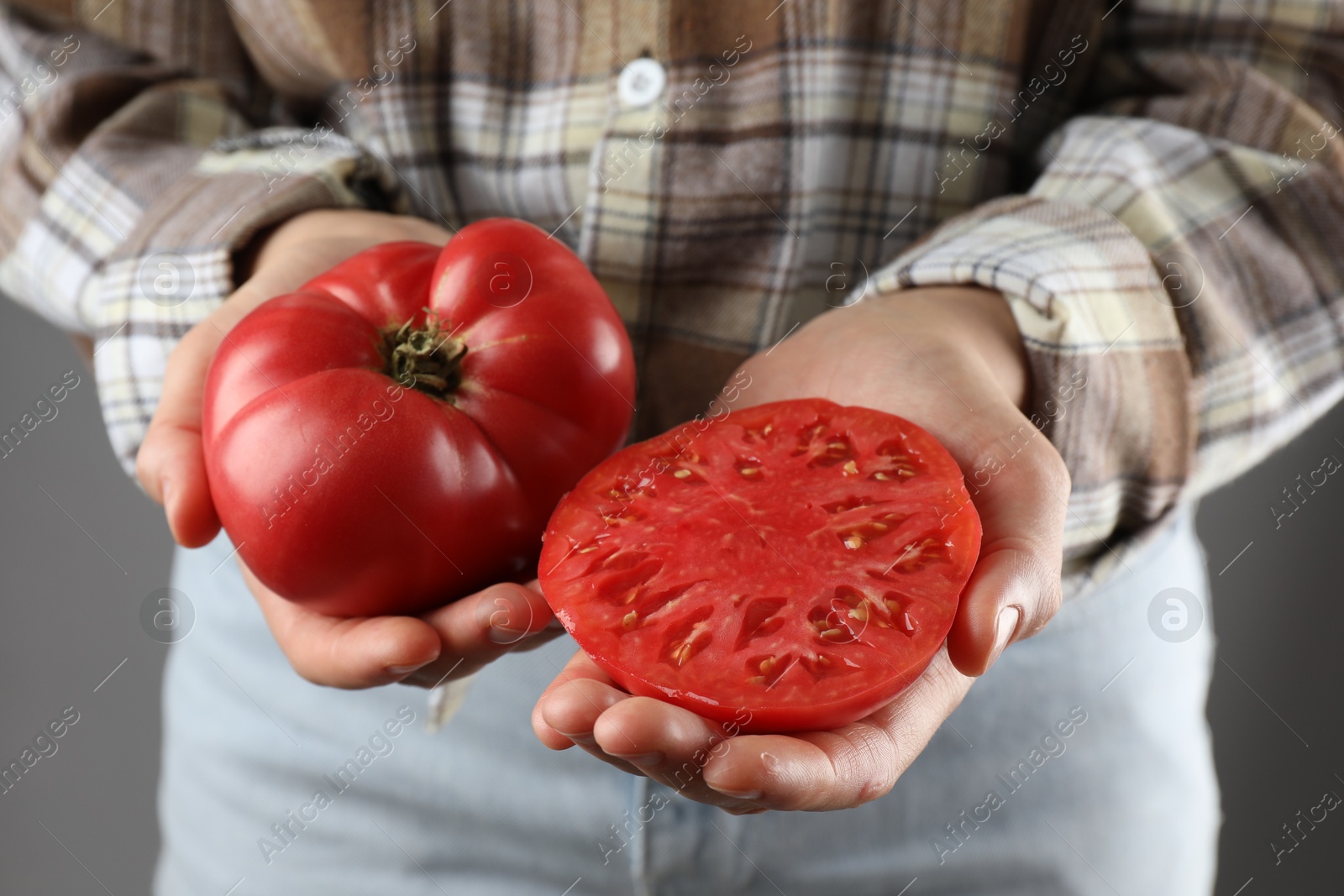 Photo of Woman holding whole and cut ripe tomatoes on grey background, closeup