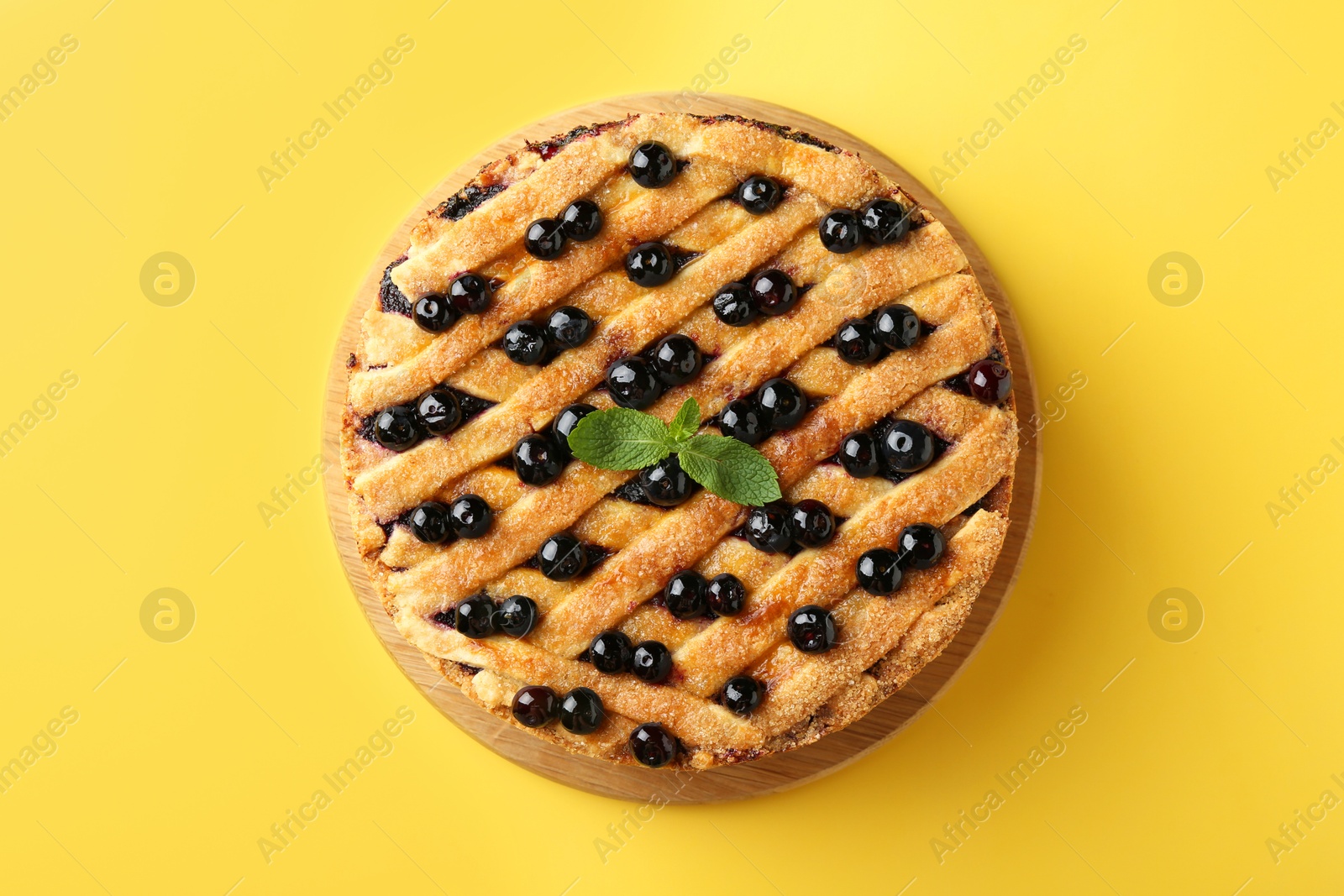 Photo of Delicious homemade blueberry pie with mint on yellow background, top view