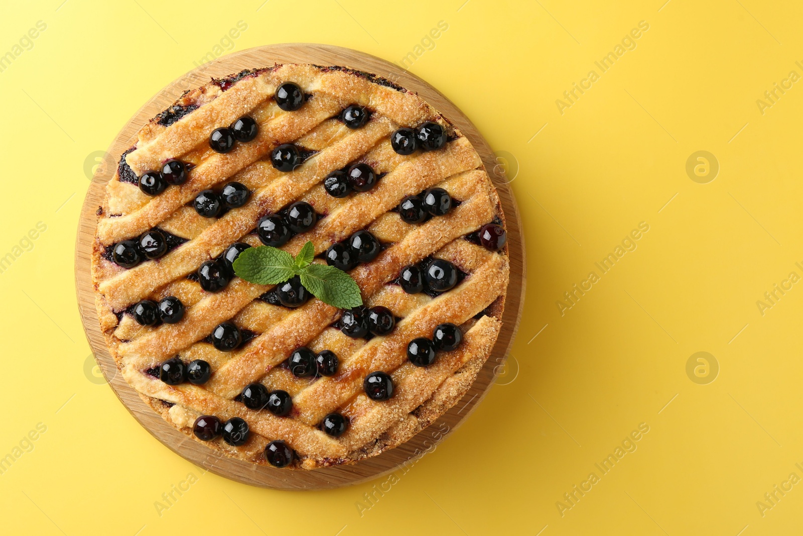 Photo of Delicious homemade blueberry pie with mint on yellow background, top view. Space for text