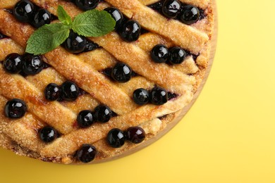 Photo of Delicious homemade blueberry pie with mint on yellow background, top view