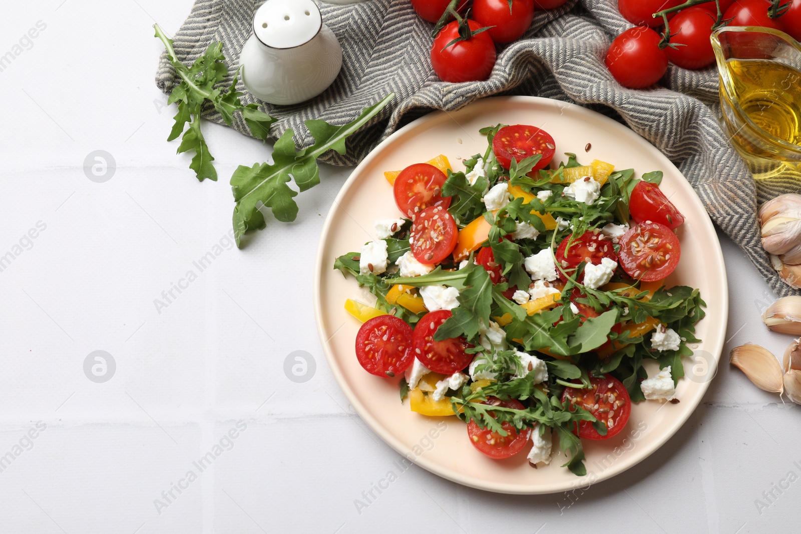 Photo of Tasty salad with arugula, cheese and vegetables on white tiled table, flat lay. Space for text