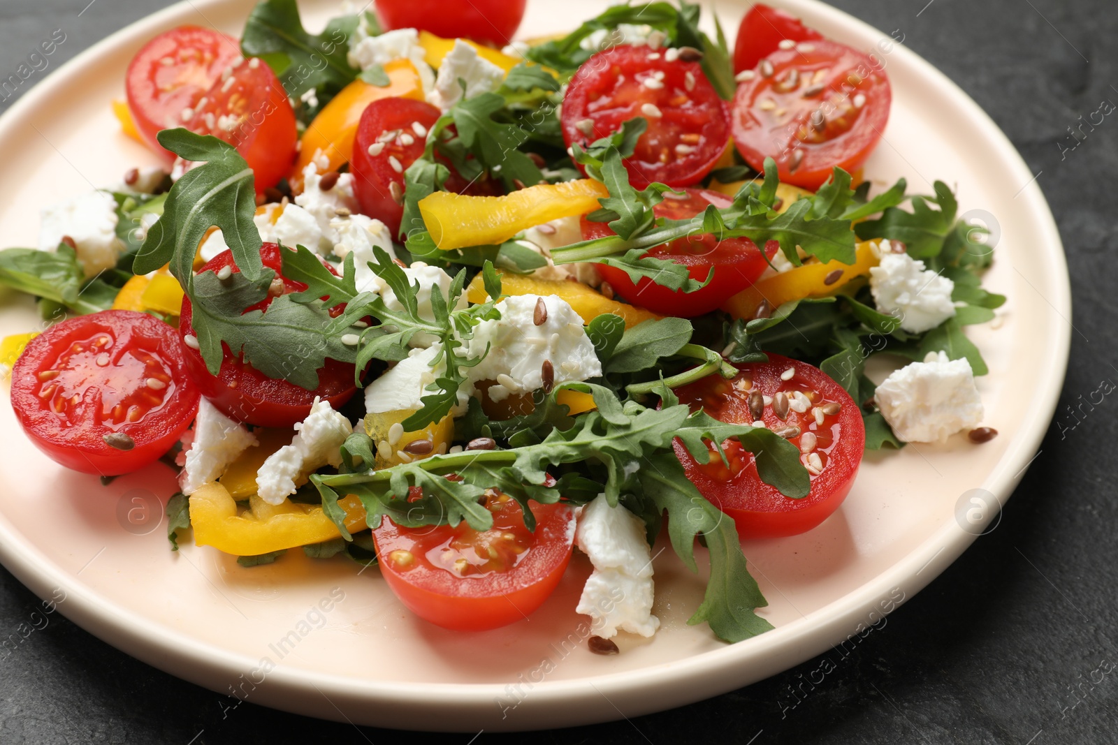 Photo of Tasty salad with arugula, cheese and vegetables on dark textured table, closeup