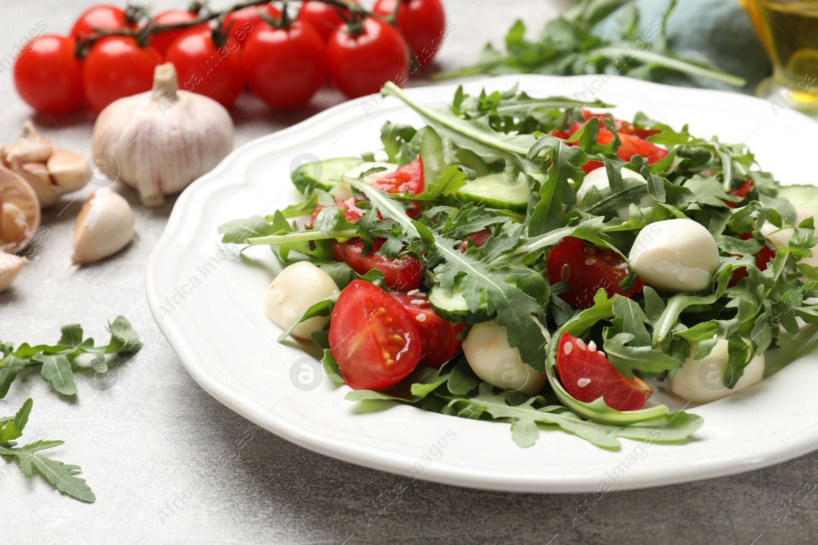 Photo of Tasty salad with arugula, mozzarella, tomatoes and cucumber on grey textured table, closeup