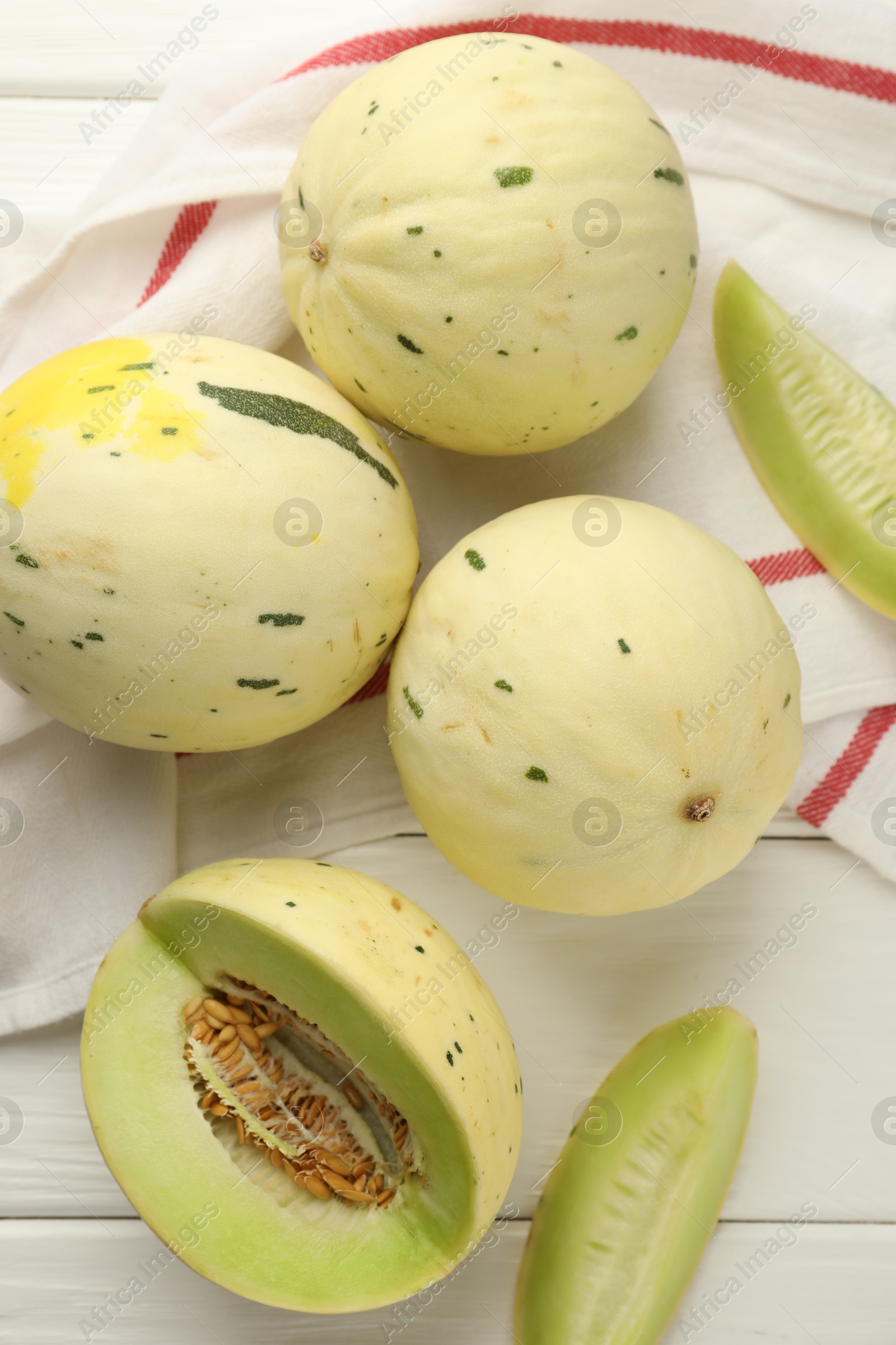 Photo of Fresh whole and cut honeydew melons on white wooden table, flat lay