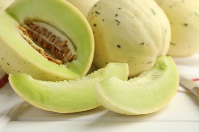 Photo of Fresh whole and cut honeydew melons on white wooden table, closeup