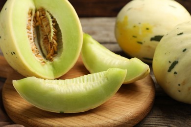 Photo of Fresh whole and cut honeydew melons on wooden table, closeup