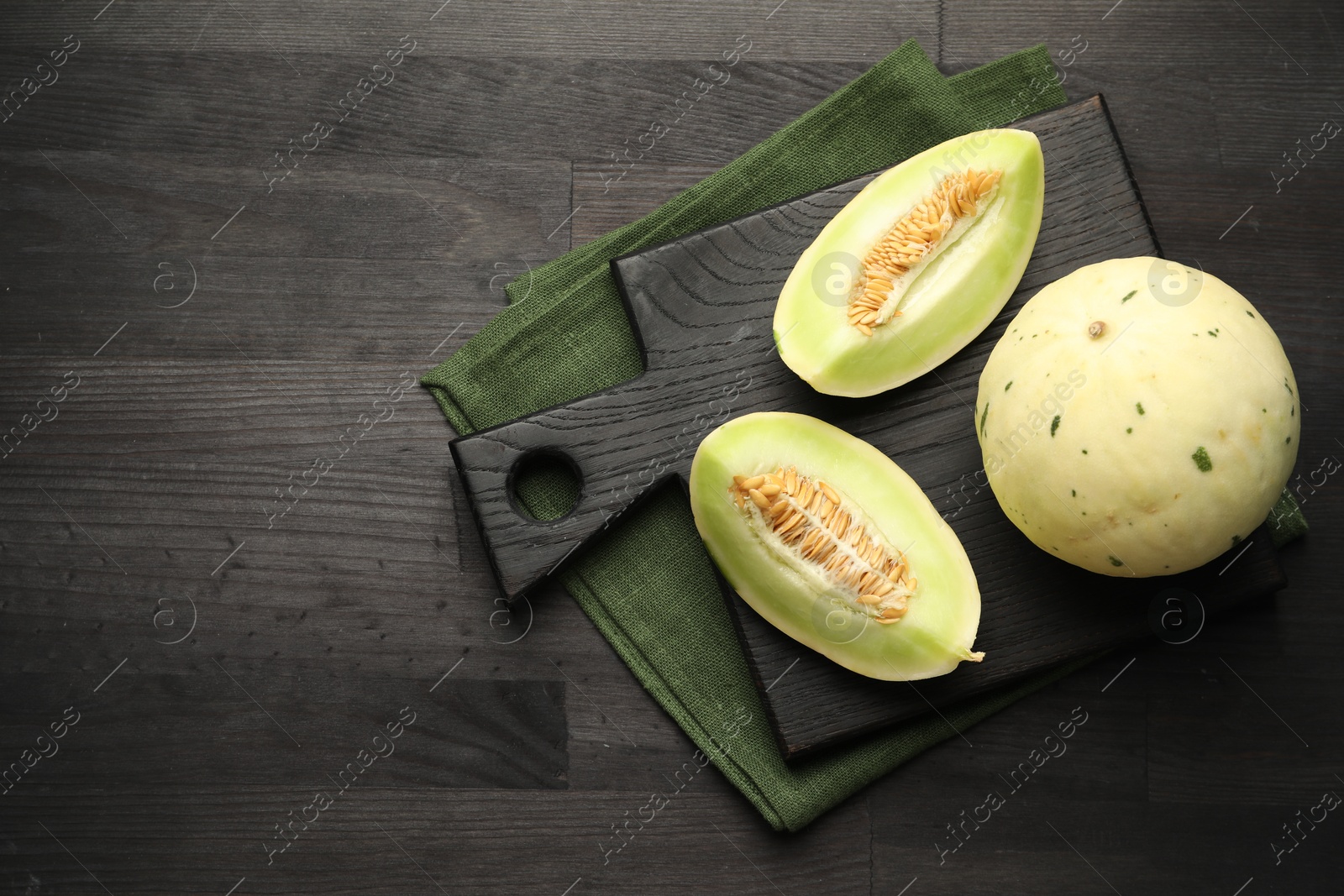 Photo of Fresh whole and cut honeydew melons on black wooden table, top view. Space for text