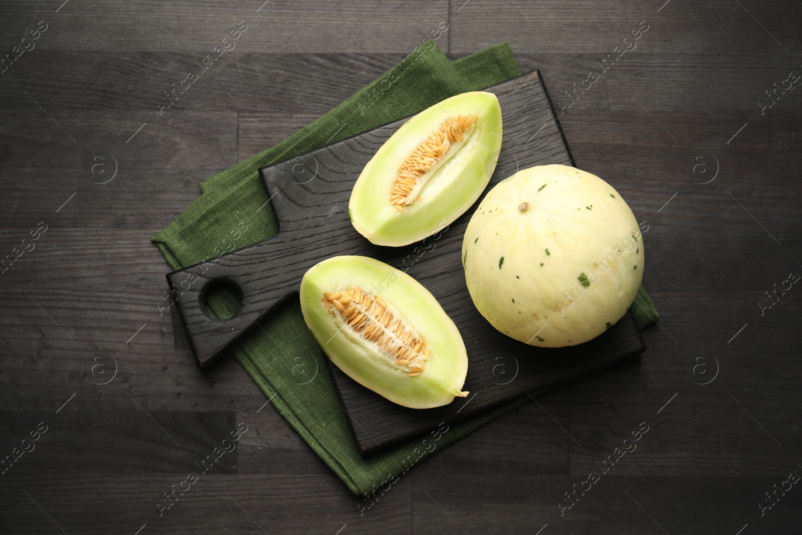 Photo of Fresh whole and cut honeydew melons on black wooden table, top view