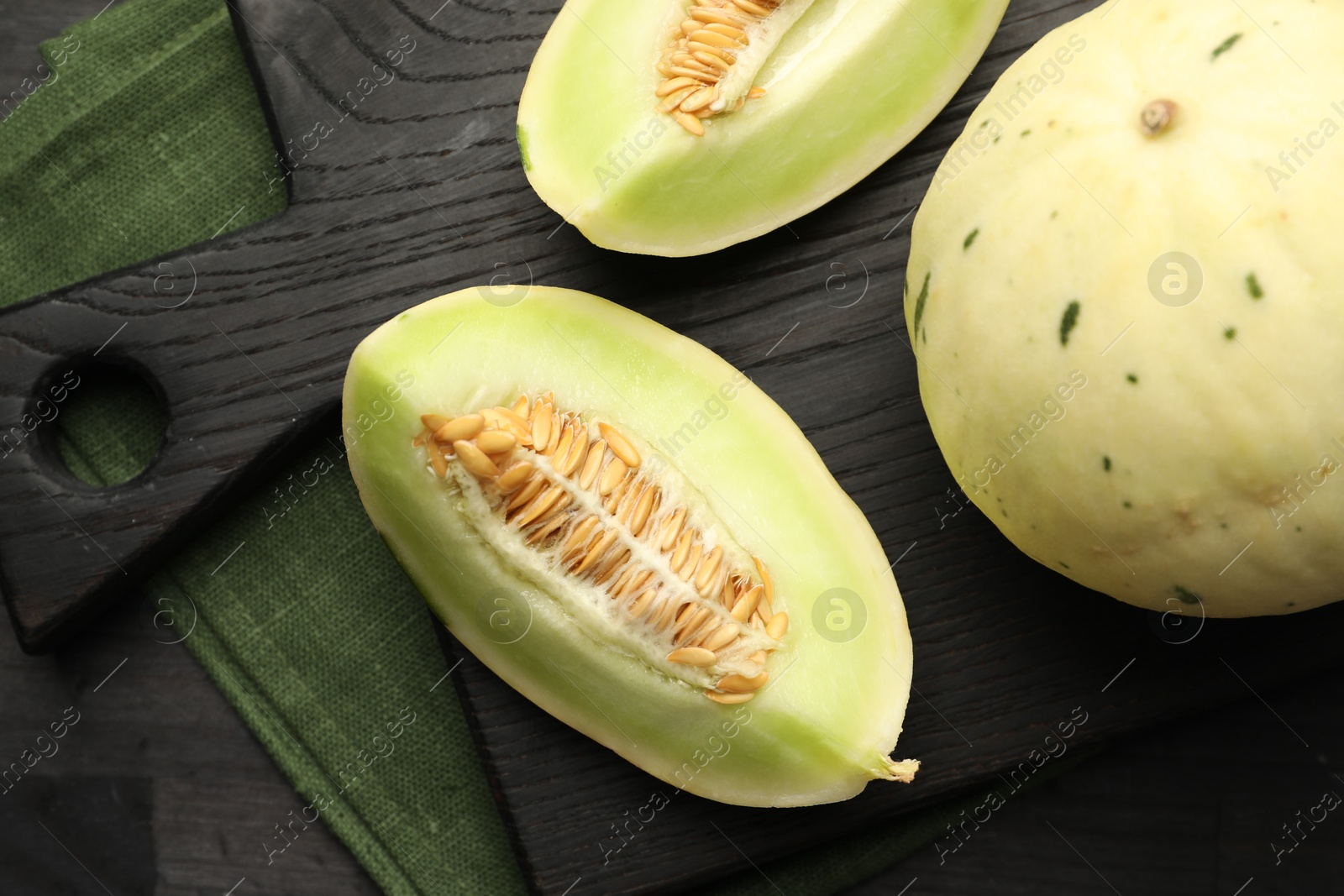 Photo of Fresh whole and cut honeydew melons on black wooden table, top view