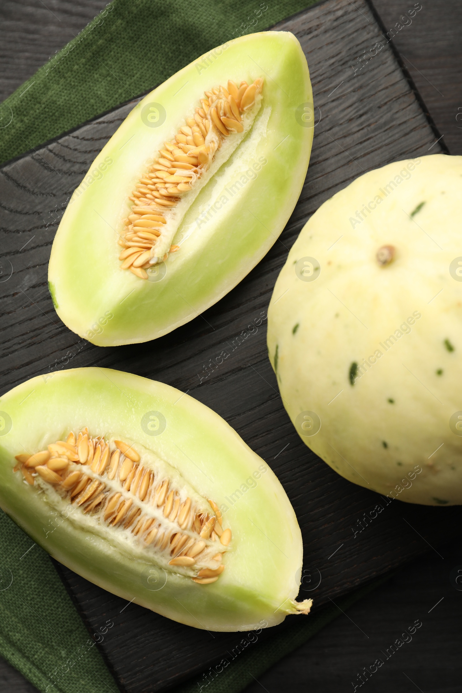 Photo of Fresh whole and cut honeydew melons on black wooden table, top view