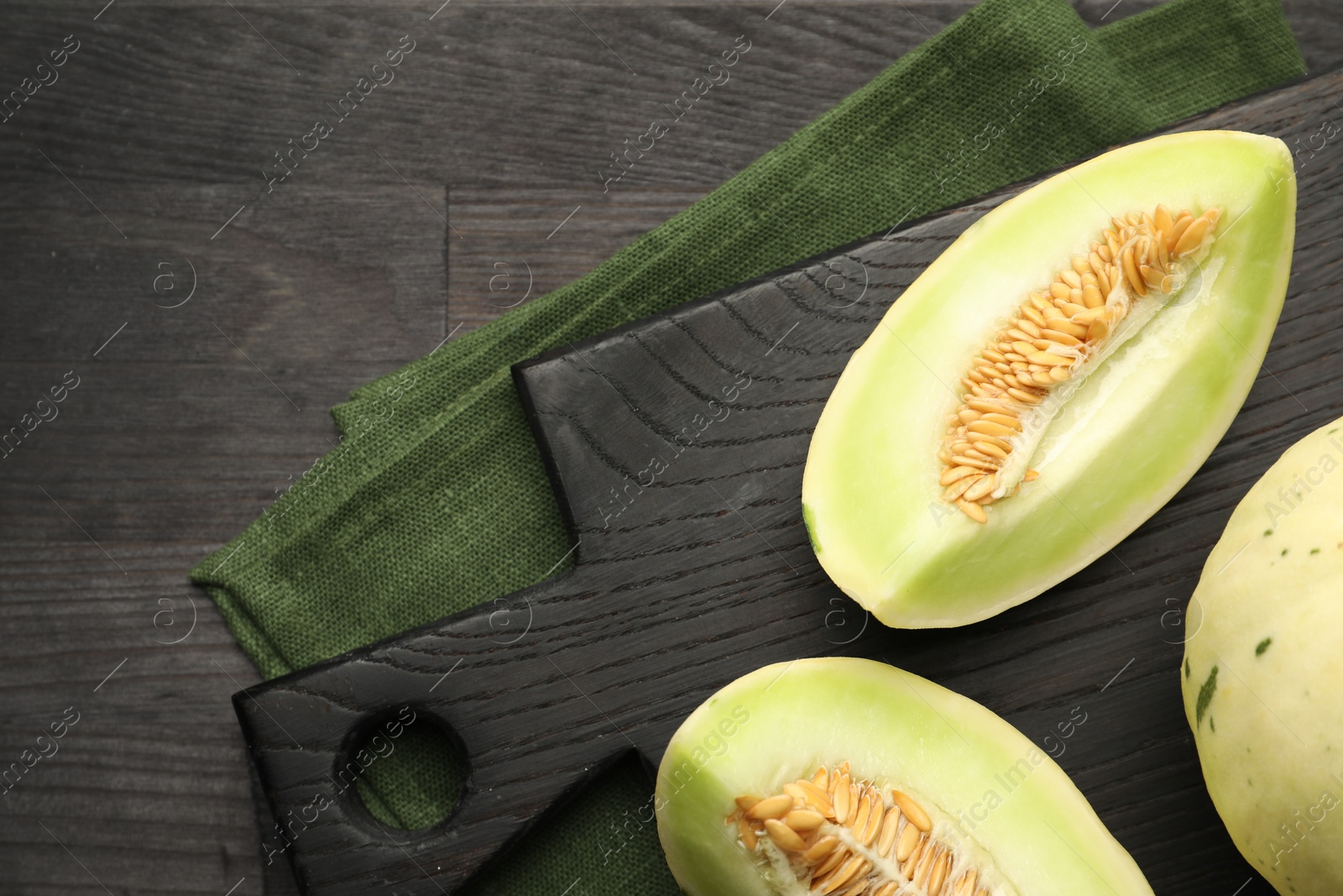 Photo of Fresh whole and cut honeydew melons on black wooden table, top view