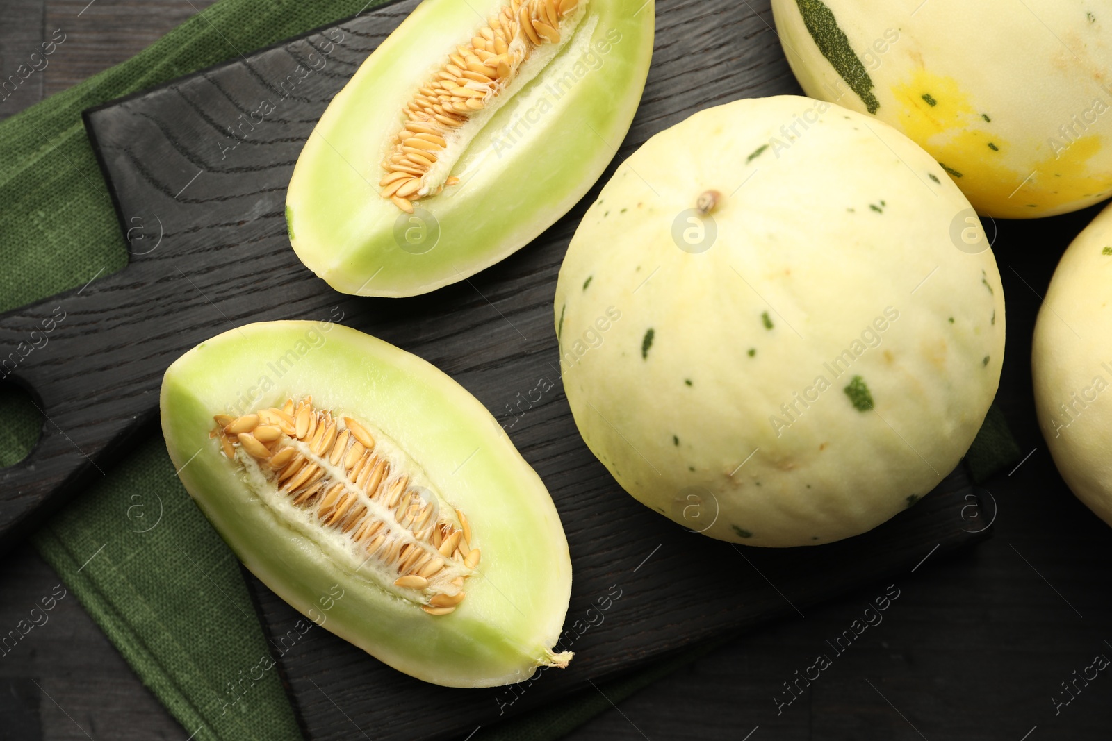 Photo of Fresh whole and cut honeydew melons on black wooden table, flat lay