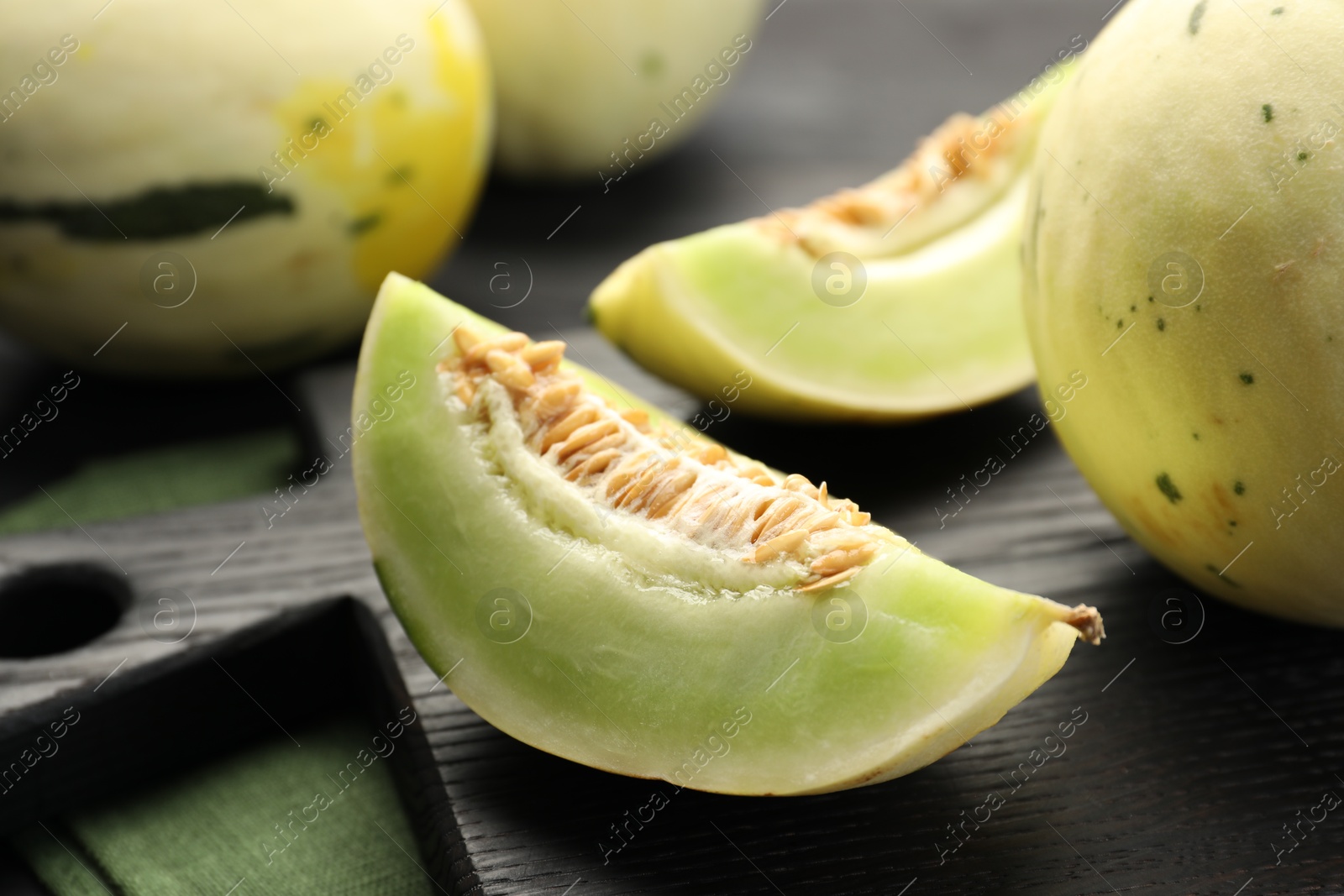 Photo of Fresh whole and cut honeydew melons on black wooden table, closeup