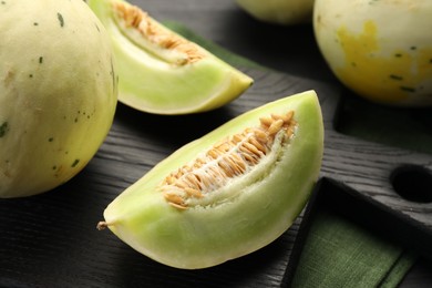 Photo of Fresh whole and cut honeydew melons on black wooden table, closeup