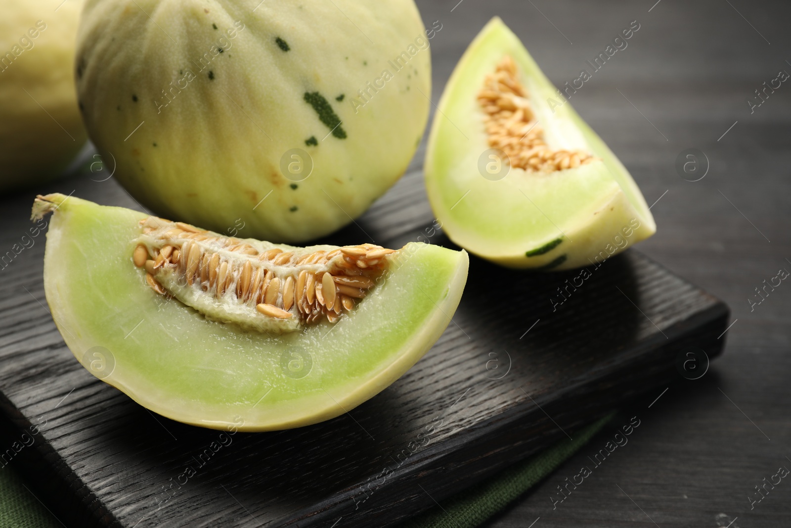 Photo of Fresh whole and cut honeydew melons on black wooden table, closeup