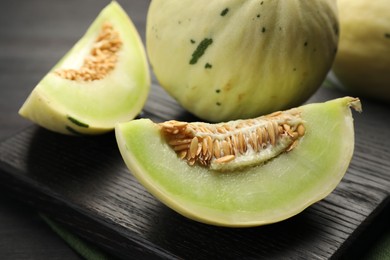 Photo of Fresh whole and cut honeydew melons on black wooden table, closeup