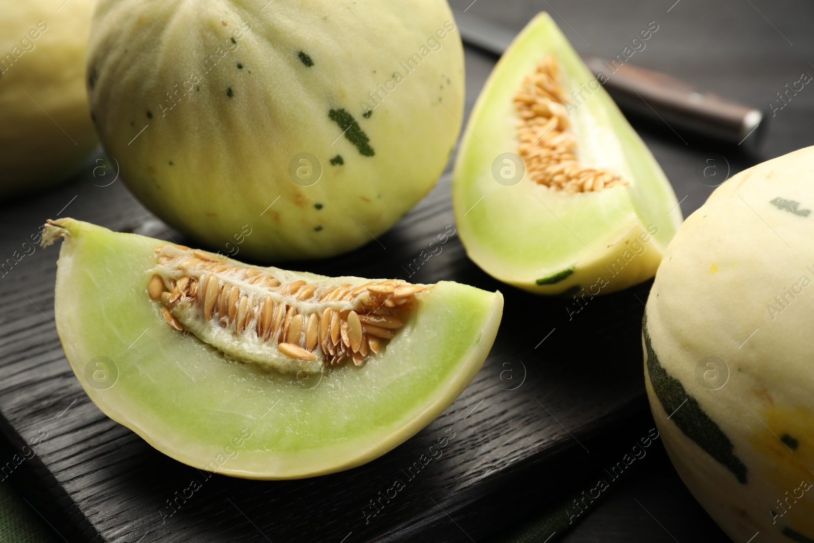 Photo of Fresh whole and cut honeydew melons on black wooden table, closeup