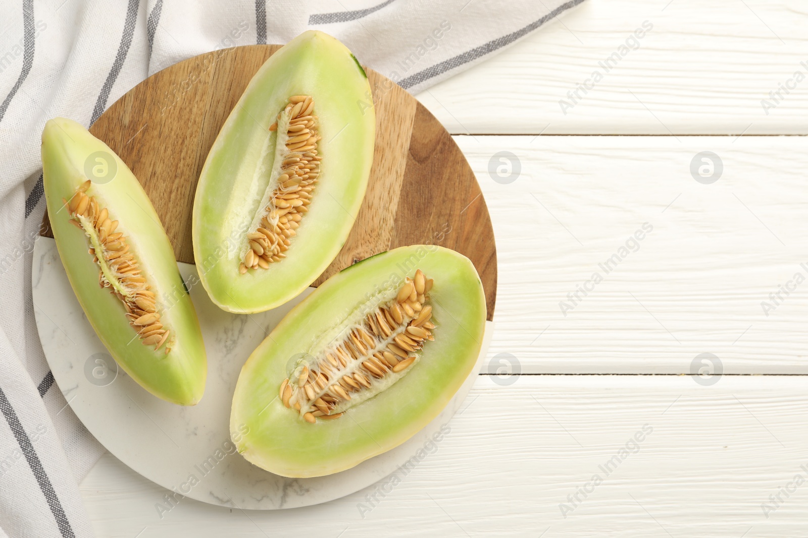 Photo of Fresh cut honeydew melon on white wooden table, top view. Space for text