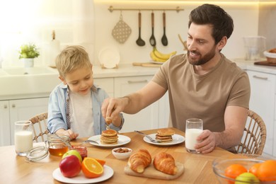 Father and his cute little son having breakfast at table in kitchen on sunny morning