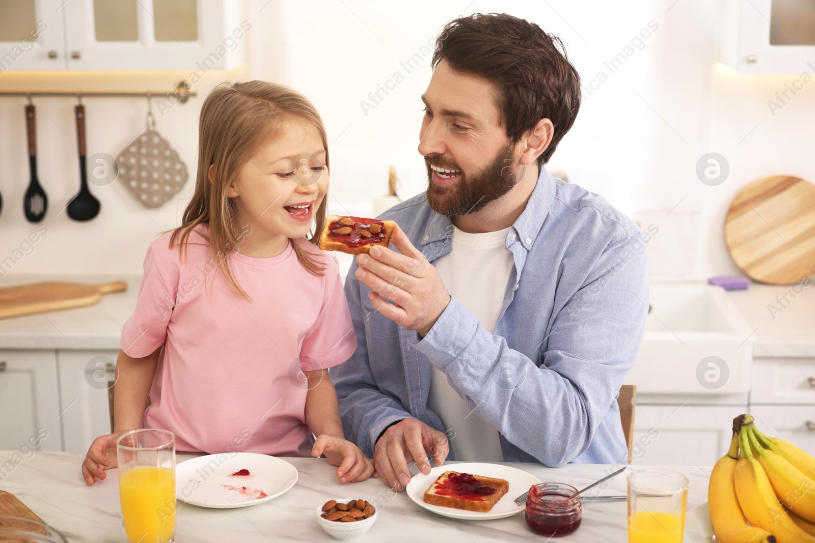 Image of Father and his cute little daughter having breakfast at table in kitchen on sunny morning