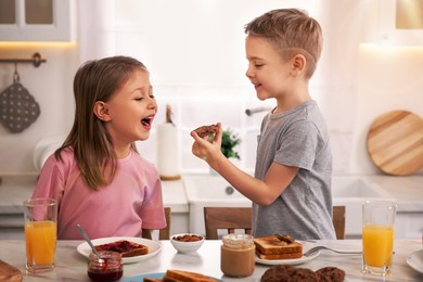 Happy siblings having breakfast at table in kitchen on sunny morning