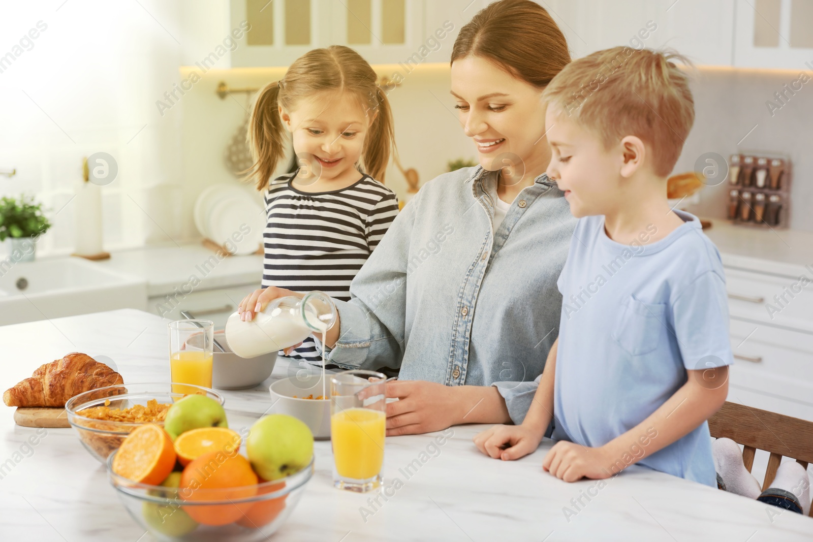 Image of Mother and her cute little children having breakfast at table in kitchen on sunny morning