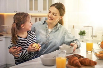 Mother and her cute little daughter having breakfast at table in kitchen on sunny morning