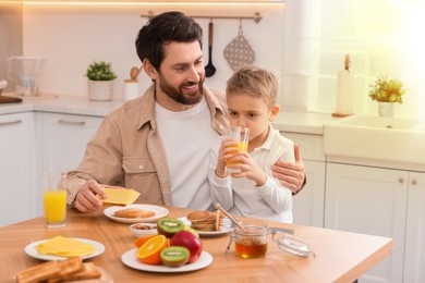 Image of Father and his cute little son having breakfast at table in kitchen on sunny morning