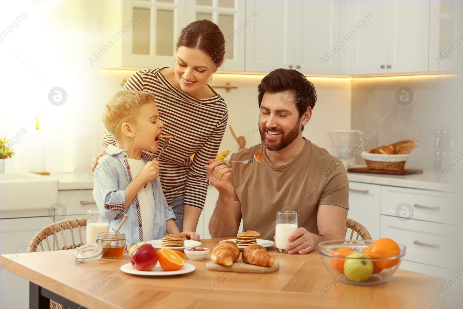 Image of Happy family having breakfast at table in kitchen on sunny morning