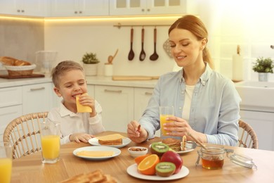 Image of Mother and her cute little son having breakfast at table in kitchen on sunny morning