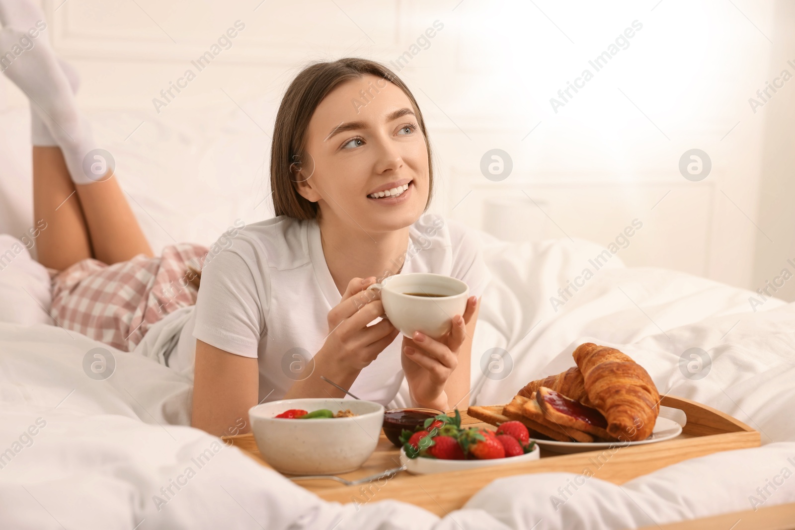 Image of Smiling woman having breakfast in bed on sunny morning