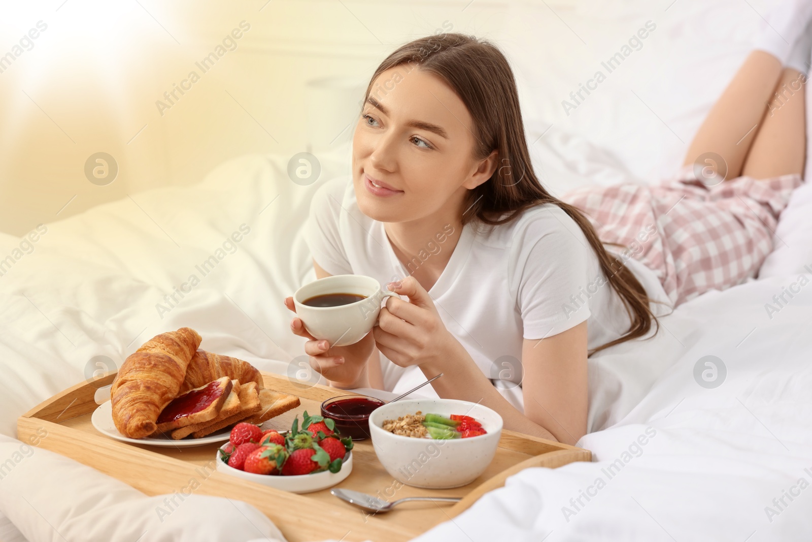 Image of Smiling woman having breakfast in bed on sunny morning