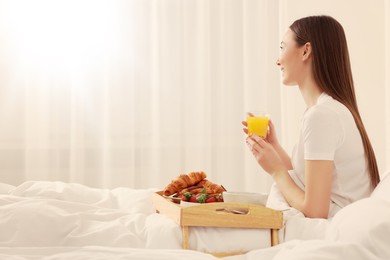 Image of Smiling woman having breakfast in bedroom on sunny morning