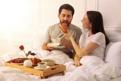 Happy couple having breakfast in bedroom on sunny morning. Space for text