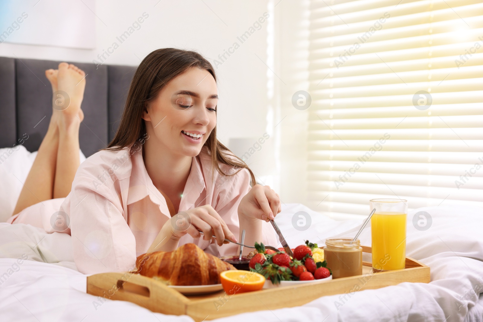 Image of Smiling woman having breakfast in bed on sunny morning